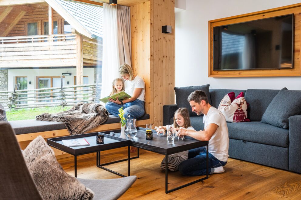 Una famiglia di quattro persone nel soggiorno di uno degli chalet della fattoria Trattler, che legge e gioca.