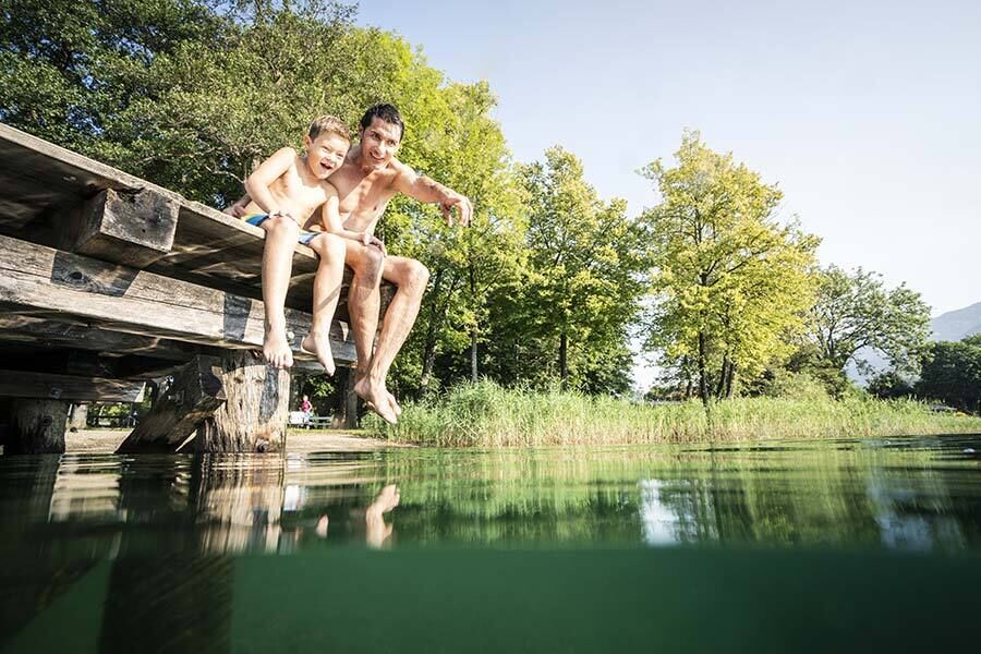 Ein Vater und sein Sohn sitzen am Steg und der Vater zeigt seinem Sohn etwas im Wasser des Millstätter Sees