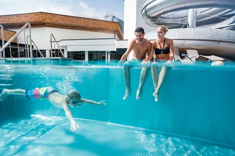 Un bambino che si tuffa nella piscina delle Terme di St Kathrein - i genitori siedono sul bordo della piscina e guardano.