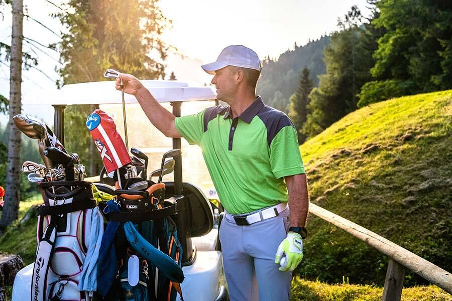 A man standing at a golf cart looking for the perfect club for the hole