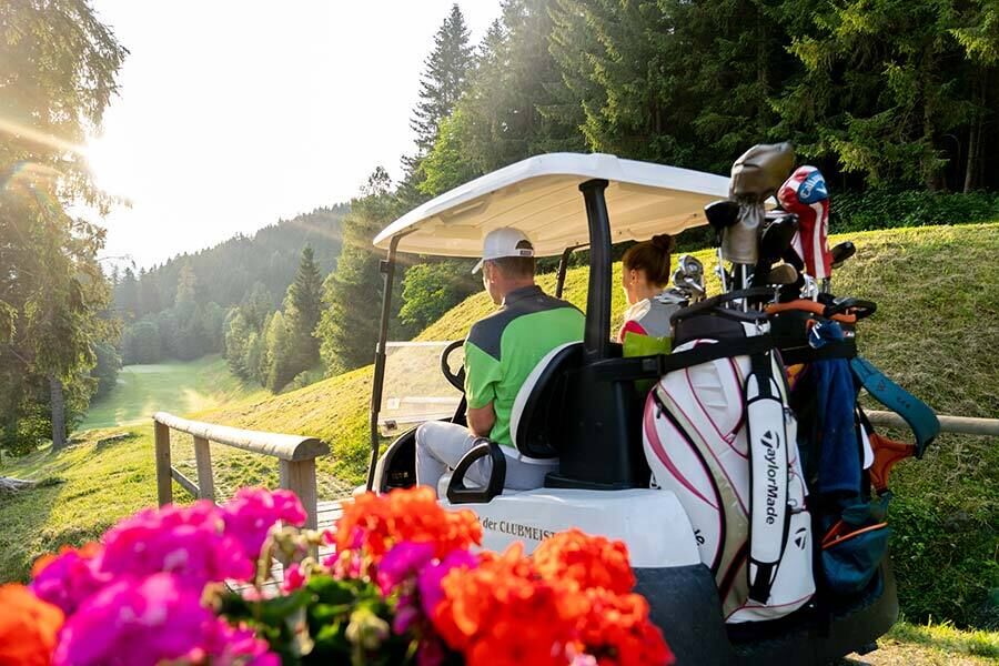 Un uomo e una donna raggiungono la prossima buca in Carinzia con un golf cart