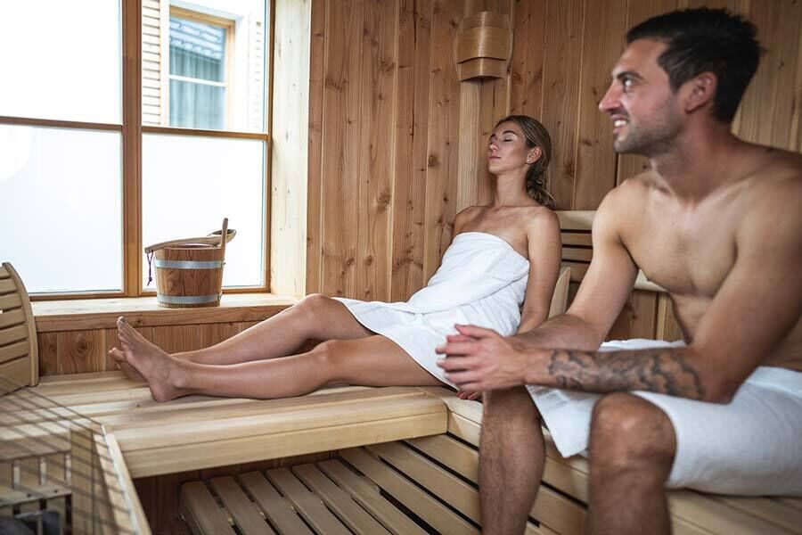 Un uomo e una donna siedono nella sauna di legno dell'Hof-Chalets in Carinzia.