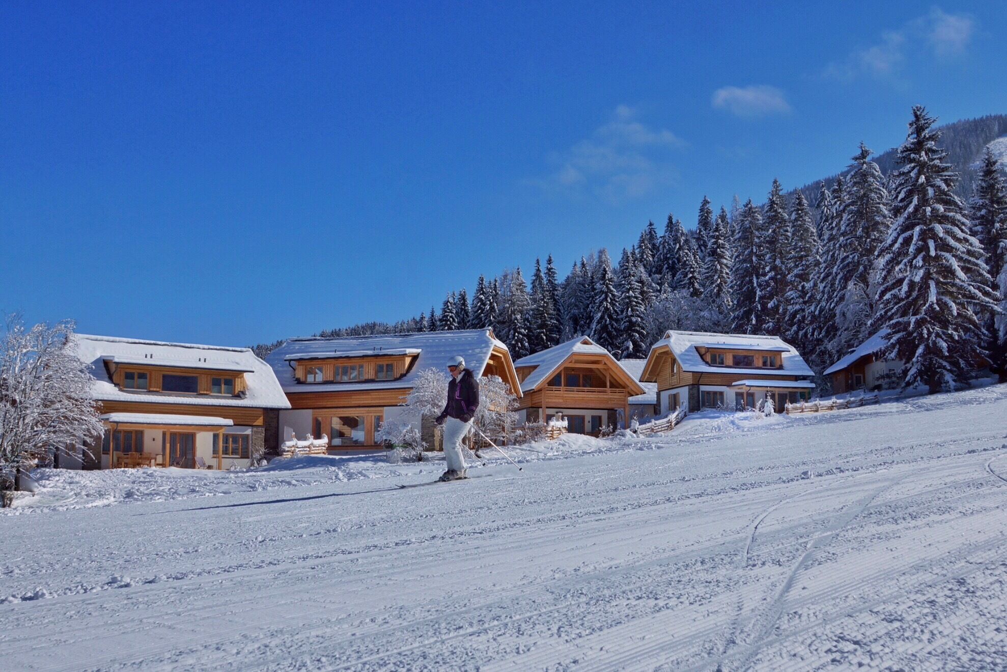 Ein Skifahrer der auf einer schön Präparierten Piste bei den Trattlershof chalets vorbeifährt.