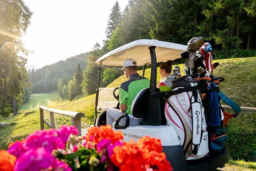 Ein Mann und eine Frau fahren mit dem Golfcart zum nächsten Loch in Kärnten