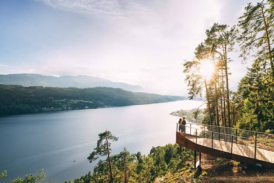 A couple stands at the top of the viewing platform admiring Lake Millstatt