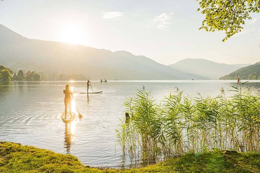 Der Millstätter See in Kärnten, inmitten von Berge. Im See haben Menschen viel Spaß beim Schwimmen und beim Stand-up-Paddeln