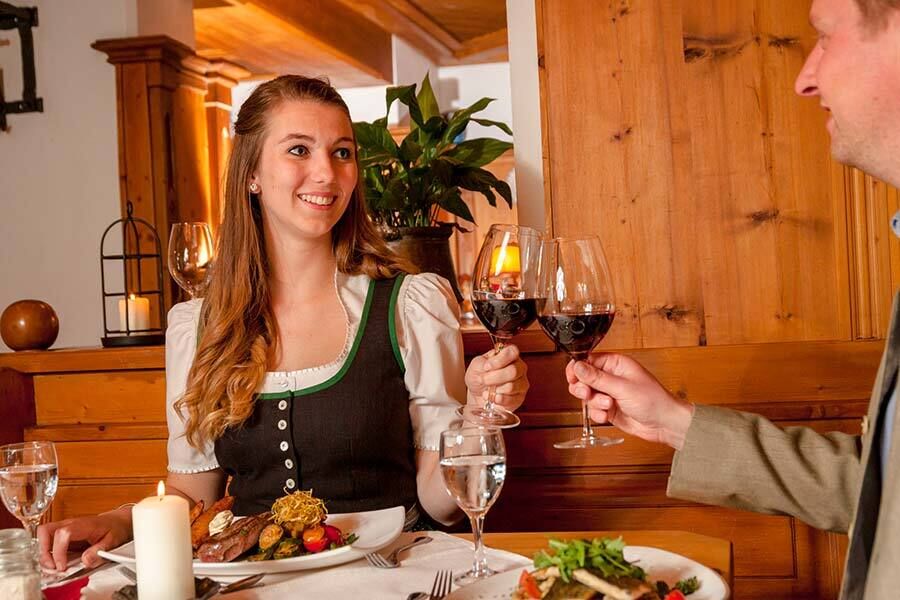 A man and a woman sit at a table and toast with a glass of red wine.