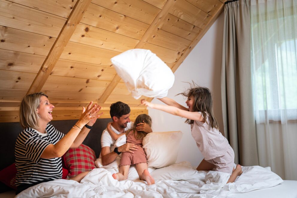 Eine vierköpfige Familie die im Trattlerhof in einem Zimmer im Bett eine Kissenschlacht macht.