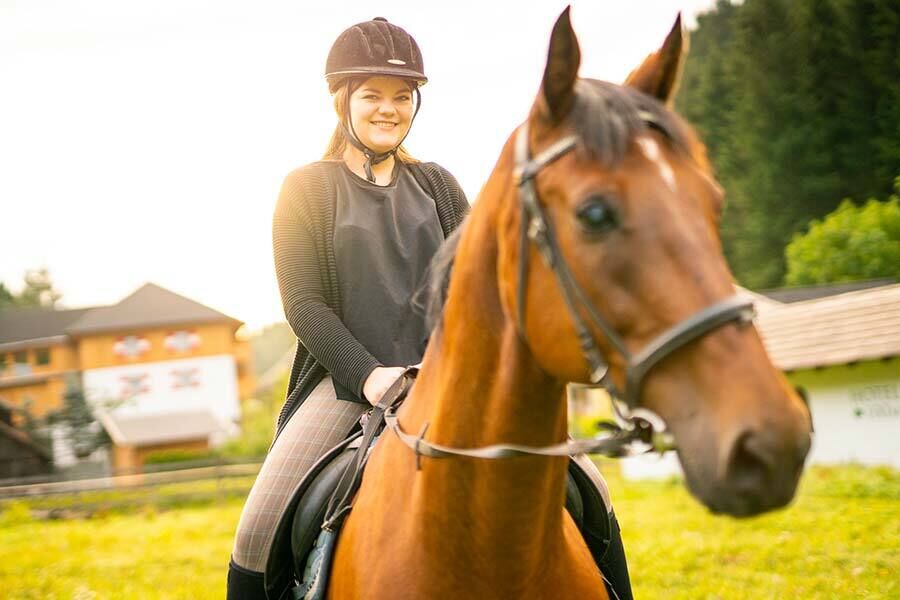 Una ragazza si siede su un cavallo marrone e cavalca in Carinzia