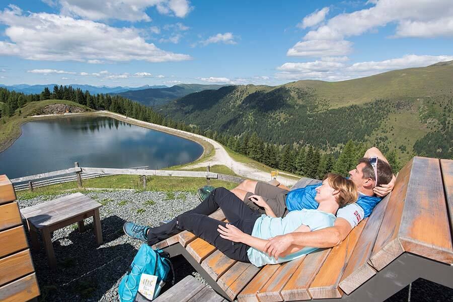 A couple lies on a wooden lounger and enjoys the view of a reservoir.