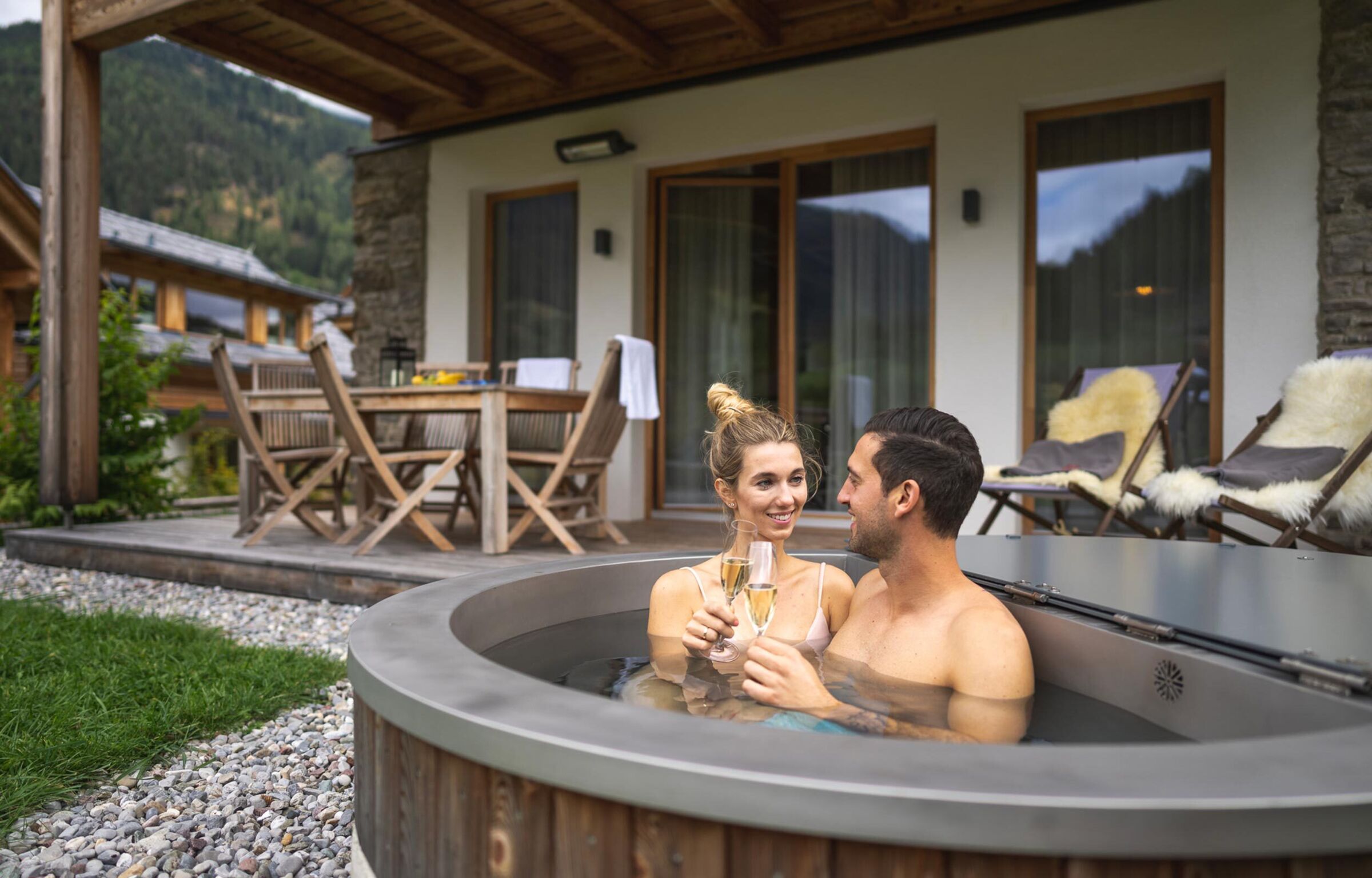 Ein Paar sitzt im Whirlpool vorm Chalet in Kärnten und trinken Sekt