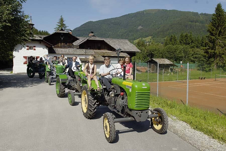 Quattro trattori Steyr d'epoca degli anni '50 percorrono una strada uno dopo l'altro, completamente occupati da bambini e adulti.