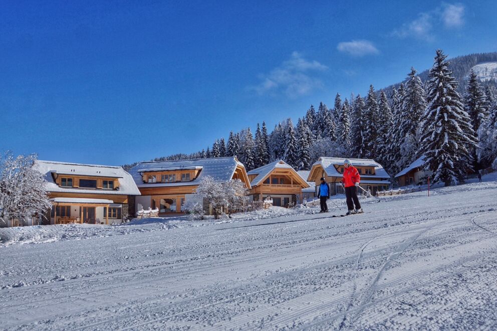 Zwei Skifahrer die im Winter an den Chalets vorbei fahren