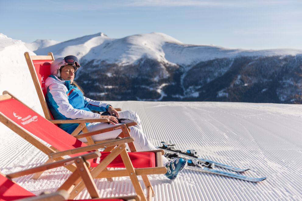 Eine Frau die eine Rast vom Skifahren macht und die Sonne im Liegestuhl genießt.