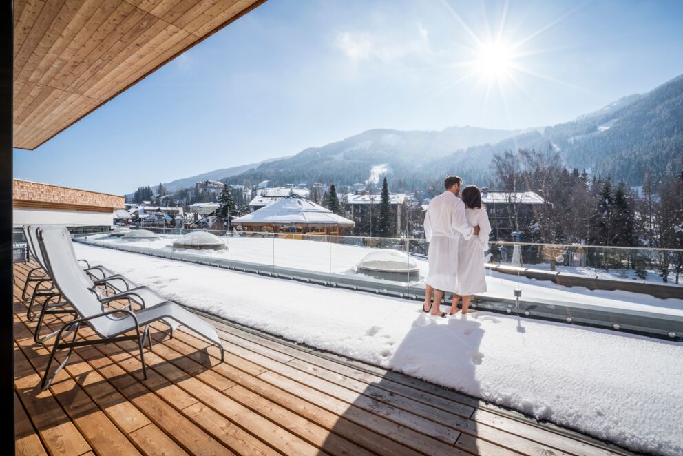 Ein Paar steht auf einer Terrasse und genießen das schöne Wetter und die wunderschöne Aussicht im Winter.