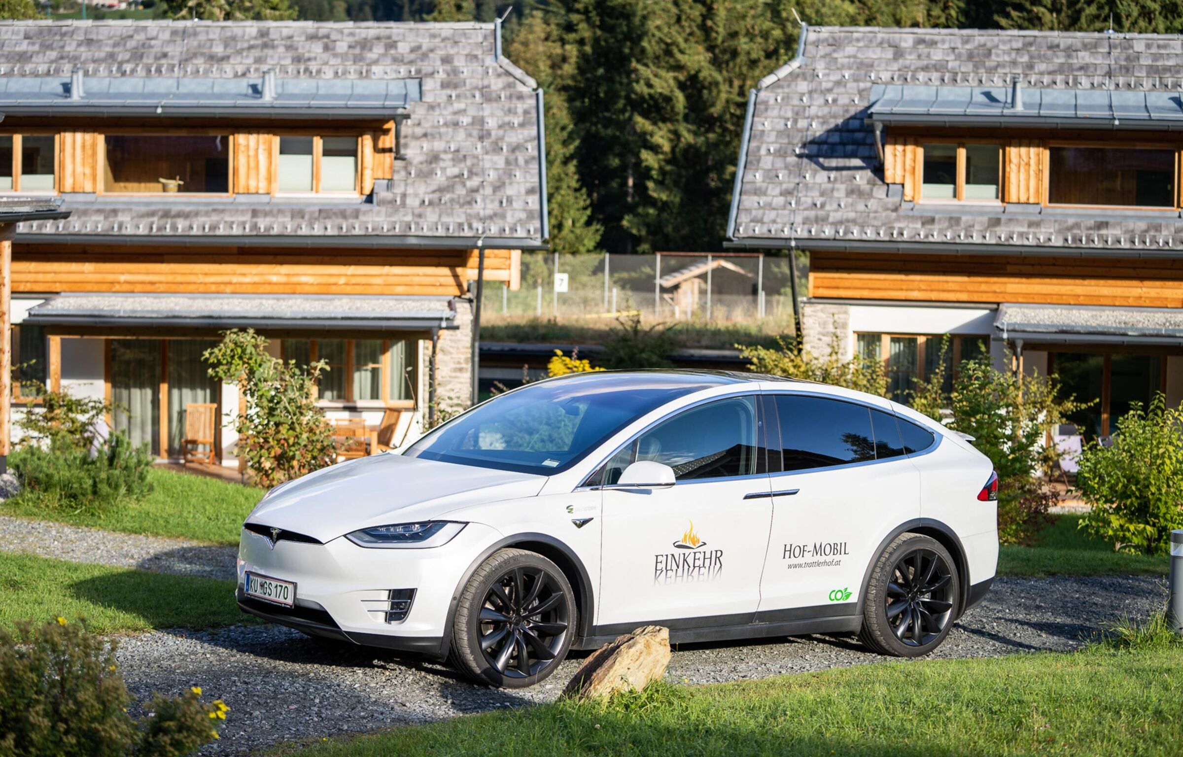 Ein weißer Tesla mit dem Trattlerhoflogo auf der Fahrertür ist auf einem Kieselweg geparkt.