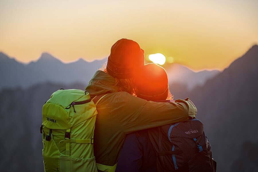 Ein sich umarmendes Paar genießt den Sonnenuntergang beim Wandern.