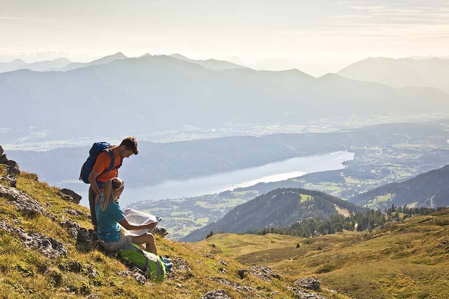 Un uomo e una donna guardano la mappa escursionistica con una splendida vista sulla Carinzia e sul lago di Millstatt