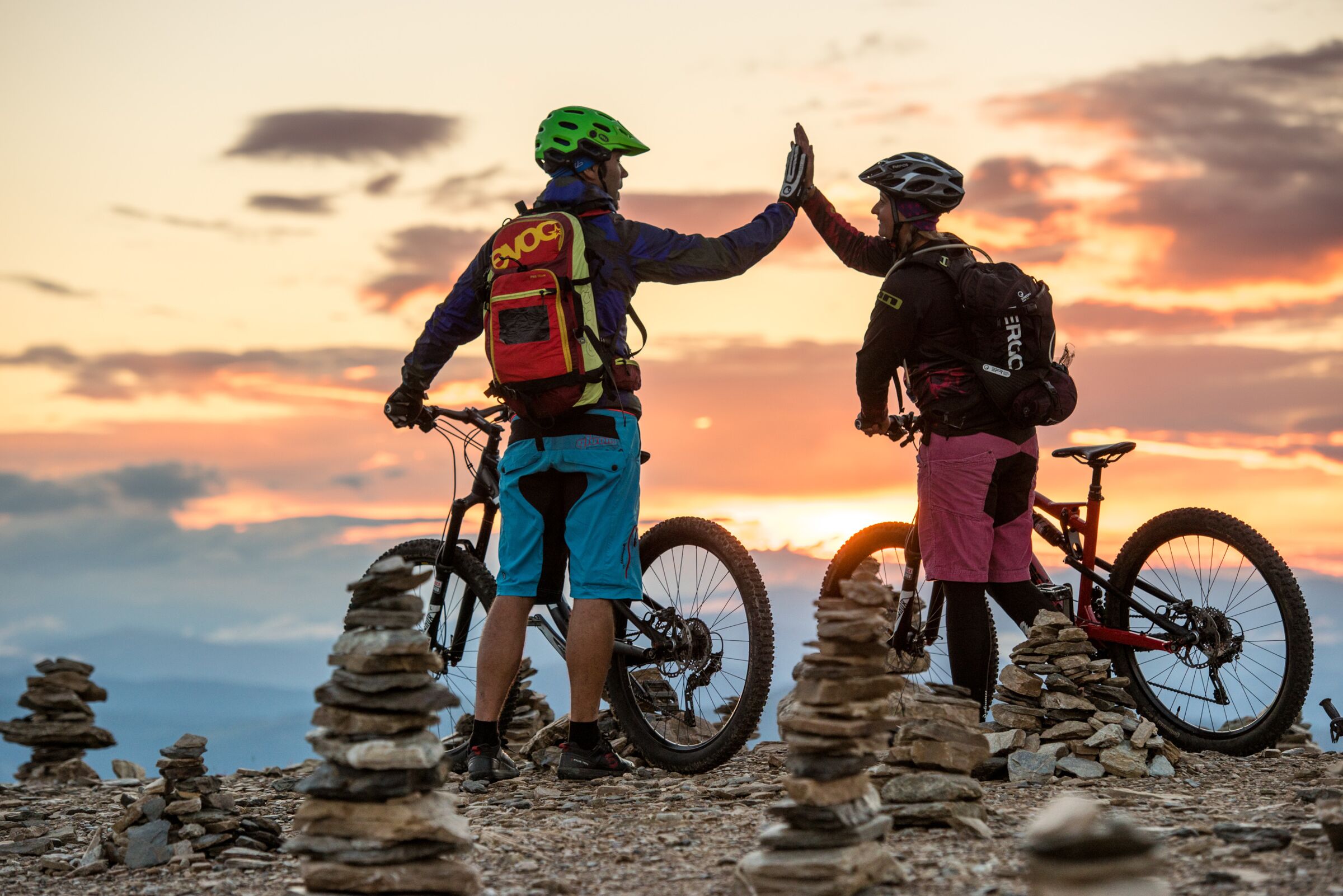 Una coppia è in piedi su una vetta con le loro mountain bike e si dà il cinque.