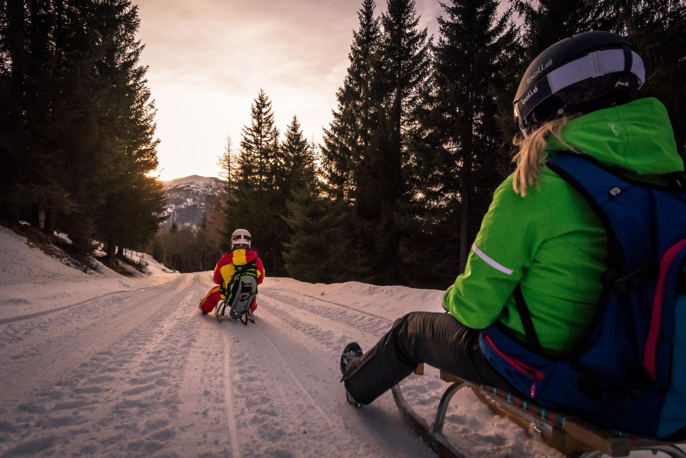 Two tobogganists on a toboggan run leading through the forest.