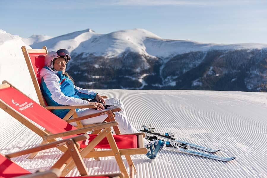 A woman in snowsuit lies on a couch on the Nockberge mountains in winter