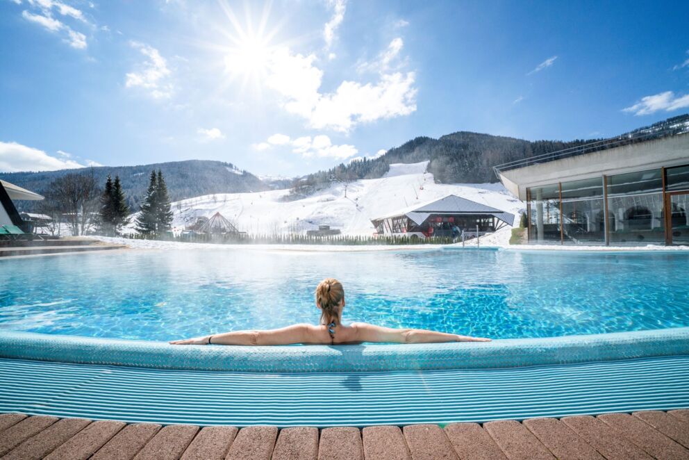 Eine Frau sitzt in einem Pool Außenbecken und blickt auf die Pisten.