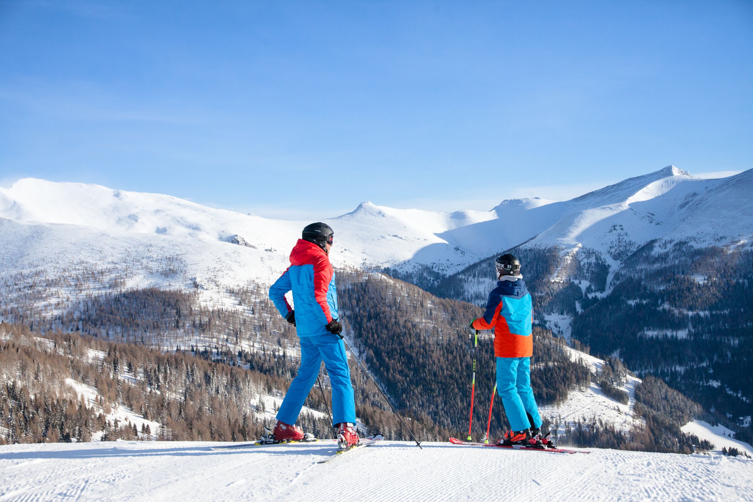 Vater und Sohn die ganz oben auf der Skipiste stehen und in die schneebedecken Berge sehen.