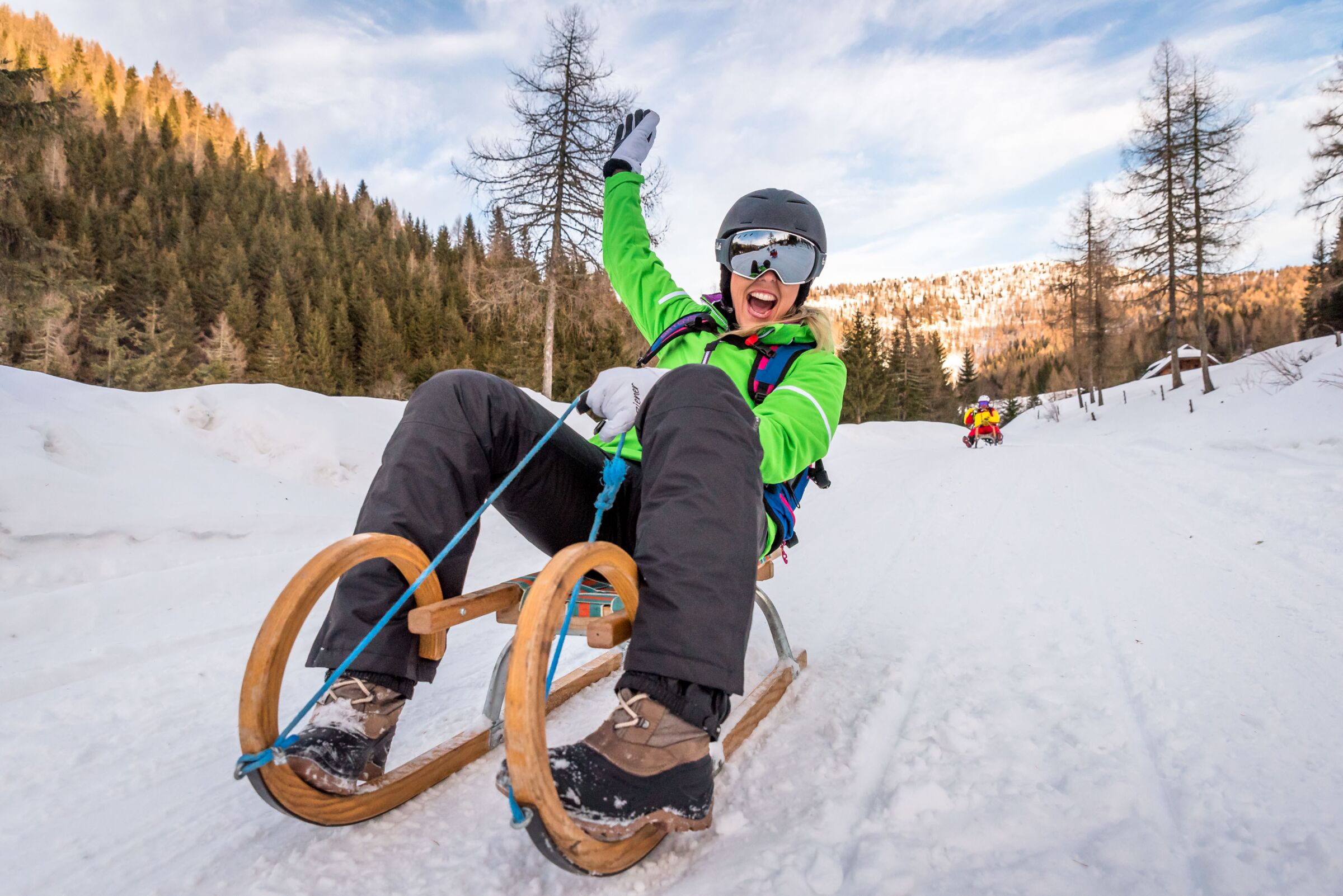 Eine Frau auf einer Rodel auf der Piste mit Wald im Hintergrund.