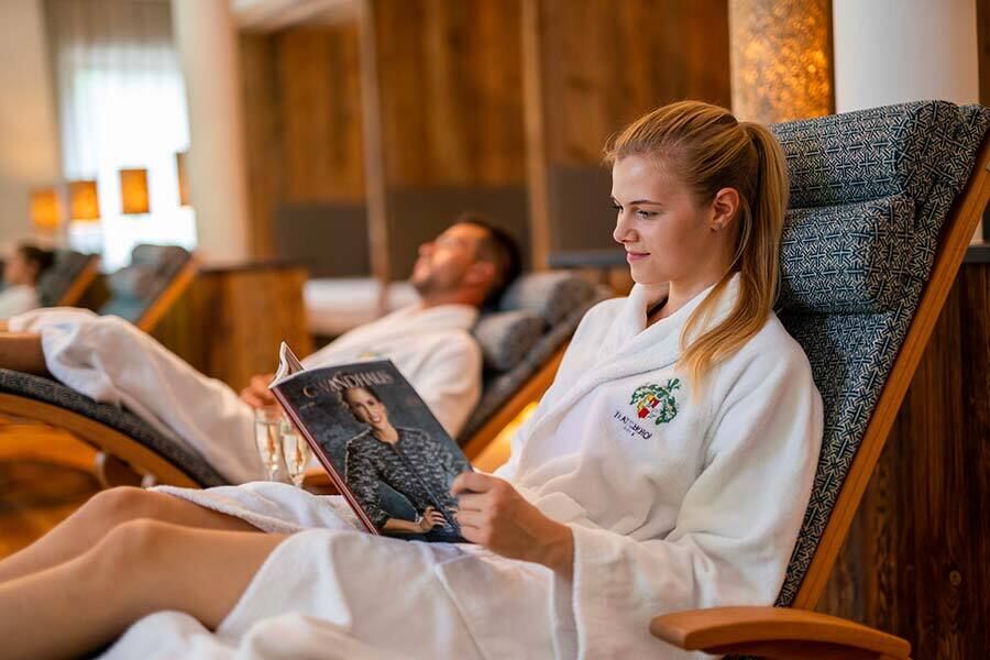 A woman sitting in a bathrobe on a comfortable armchair swing reading a magazine in the Trattlerhof relaxation room.