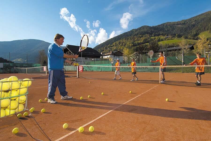 Ein Tennislehrer lernt seinen Schülern Tennis, auf dem Boden liegen bereits ein paar Tennisbälle