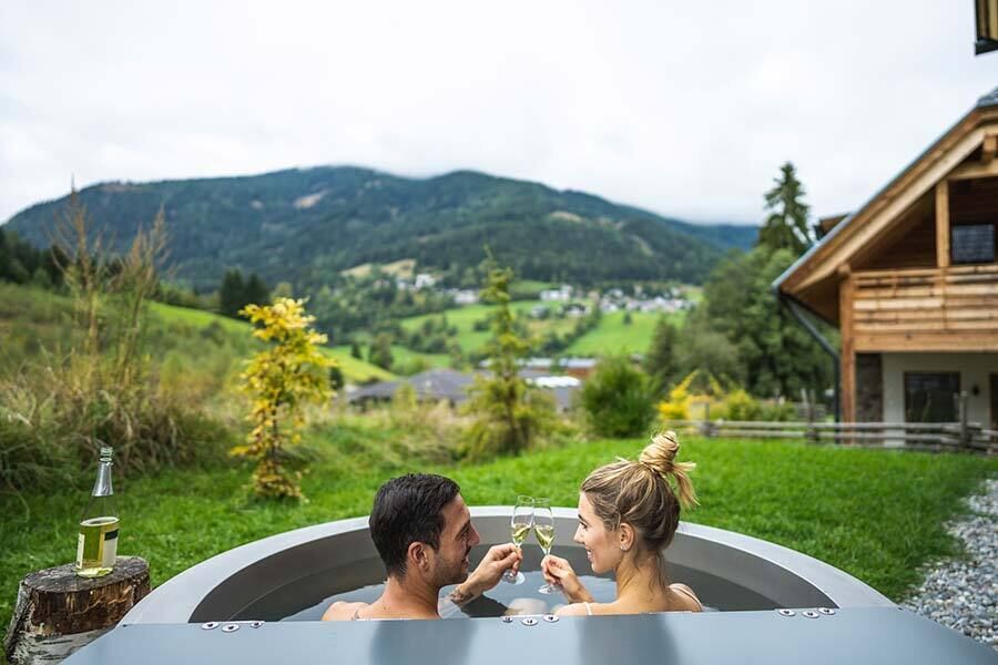A couple sits in the jacuzzi drinking sparkling wine, with an incredible view of the mountains of Carinthia