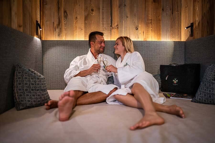 A couple in bathrobes relax with a glass of champagne in a cozy, padded sitting area