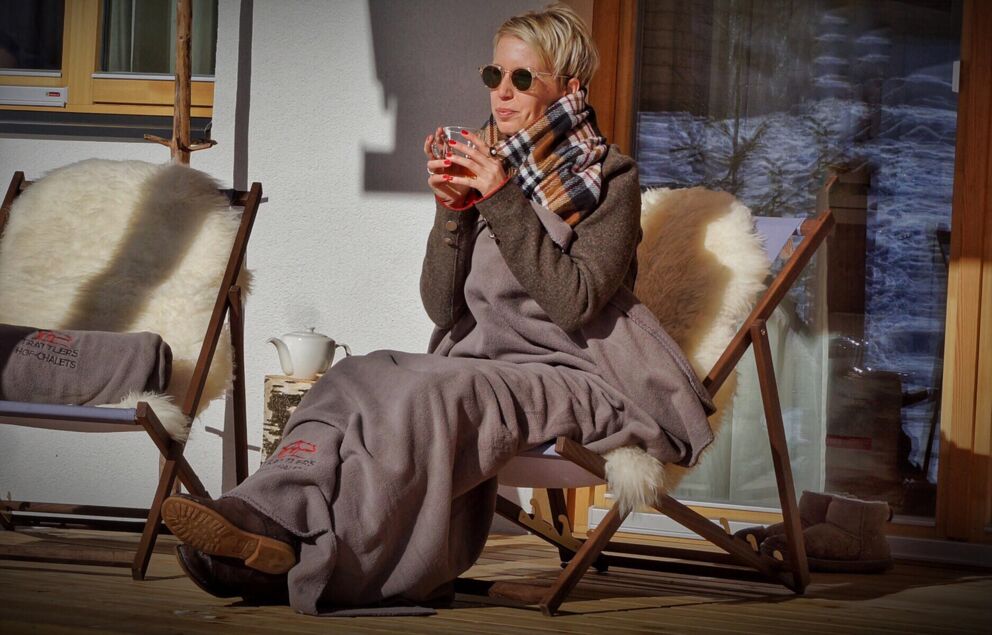 A woman sits in front of a chalet in Carinthia and drinks a warm beverage