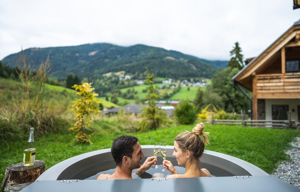 Ein Paar sitzt im Whirlpool vorm Chalet in Kärnten und trinken Sekt