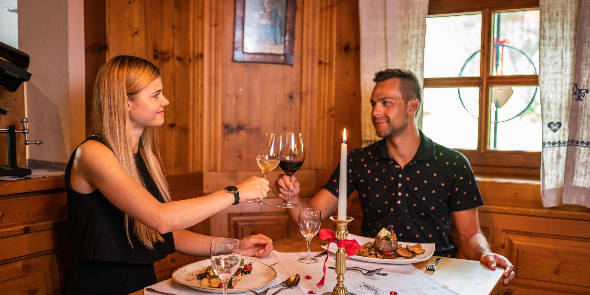 Ein Pärchen das bei einen romantischen essen mit Kerzenlicht mit Weingläsern in der Trattlers Einkehr anstößt.