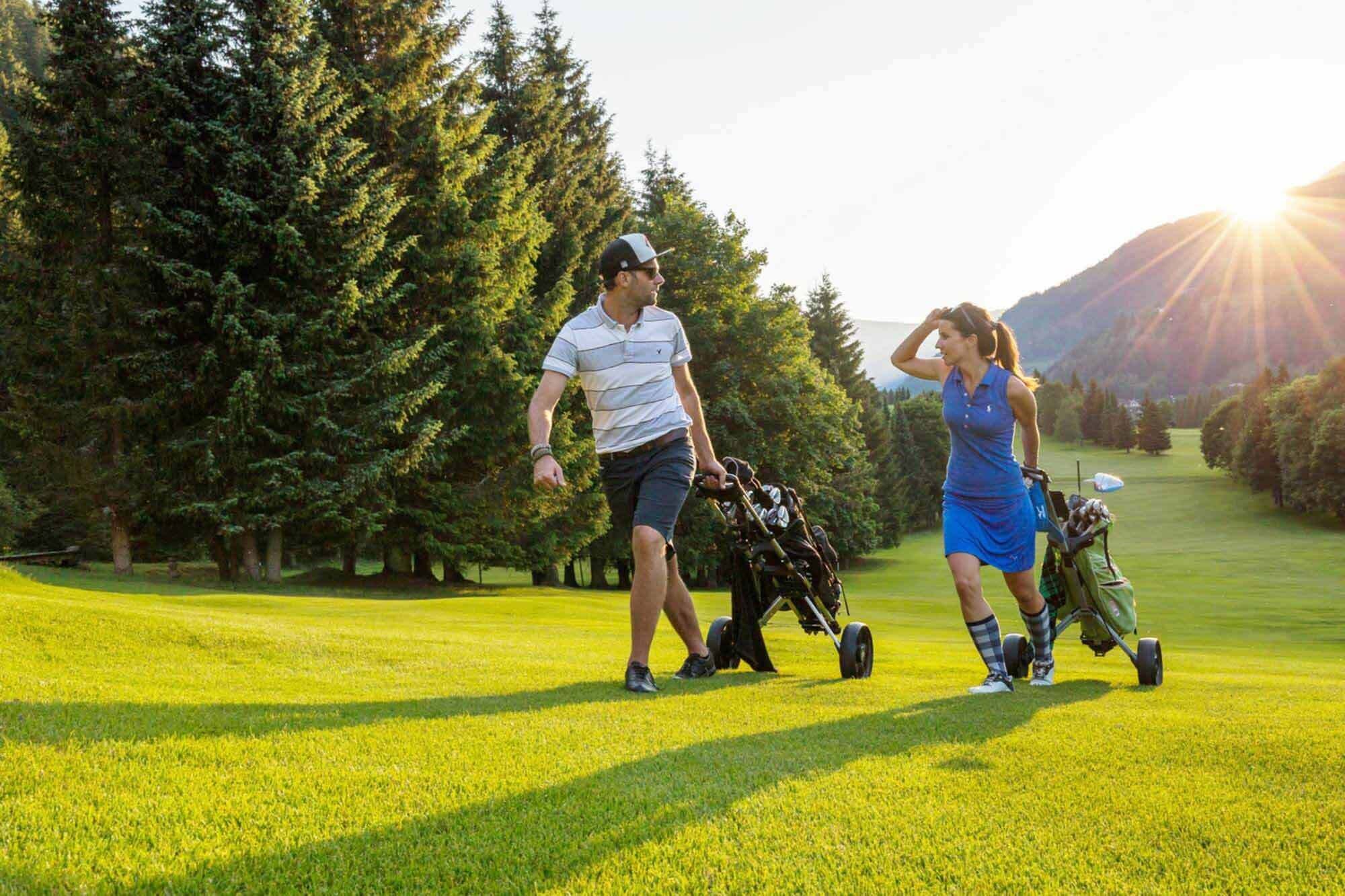 Two people walk the golf carts up a hill at the golf course in Carinthia