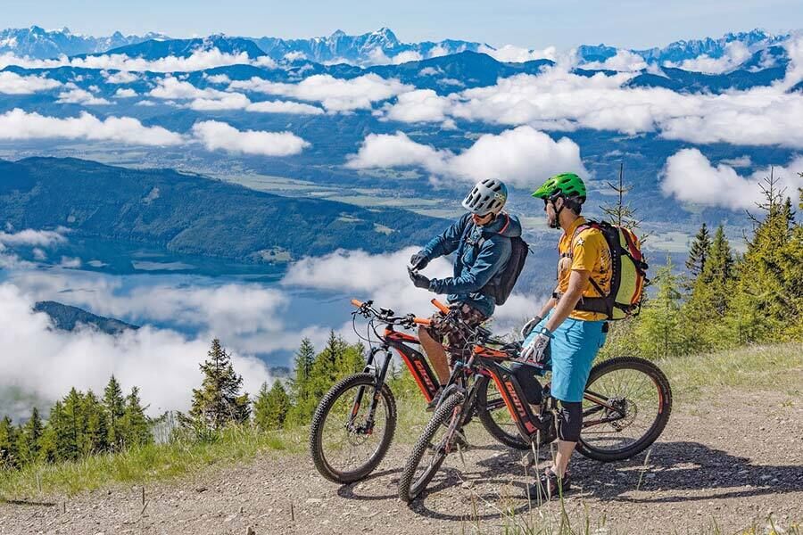 Due ciclisti si fermano lungo la strada per parlare al cellulare, mentre alle loro spalle si apre la valle e le nuvole