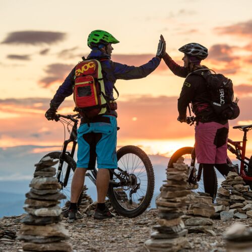 A couple is standing on a peak with their mountain bikes, high-fiving.
