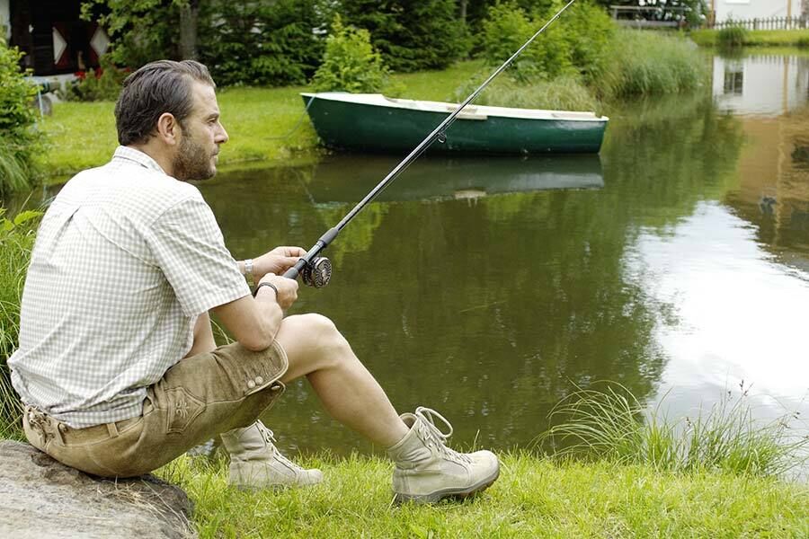 A man in traditional costume sits next to a pond and tries to catch a few fishes