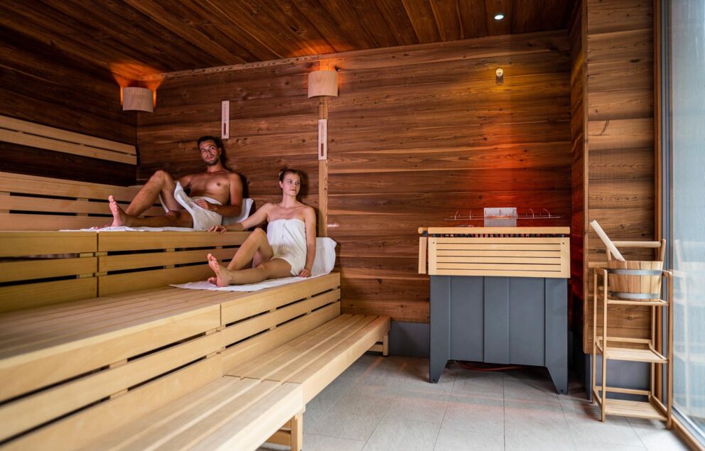 Un uomo e una donna siedono nella sauna di legno degli chalet del Trattlerhof in Carinzia.