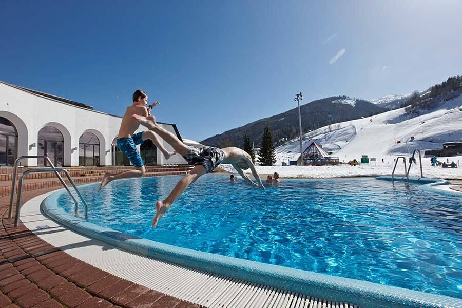 Two boys jump into the blue thermal water in the thermal Römerbad in Carinthia in winter