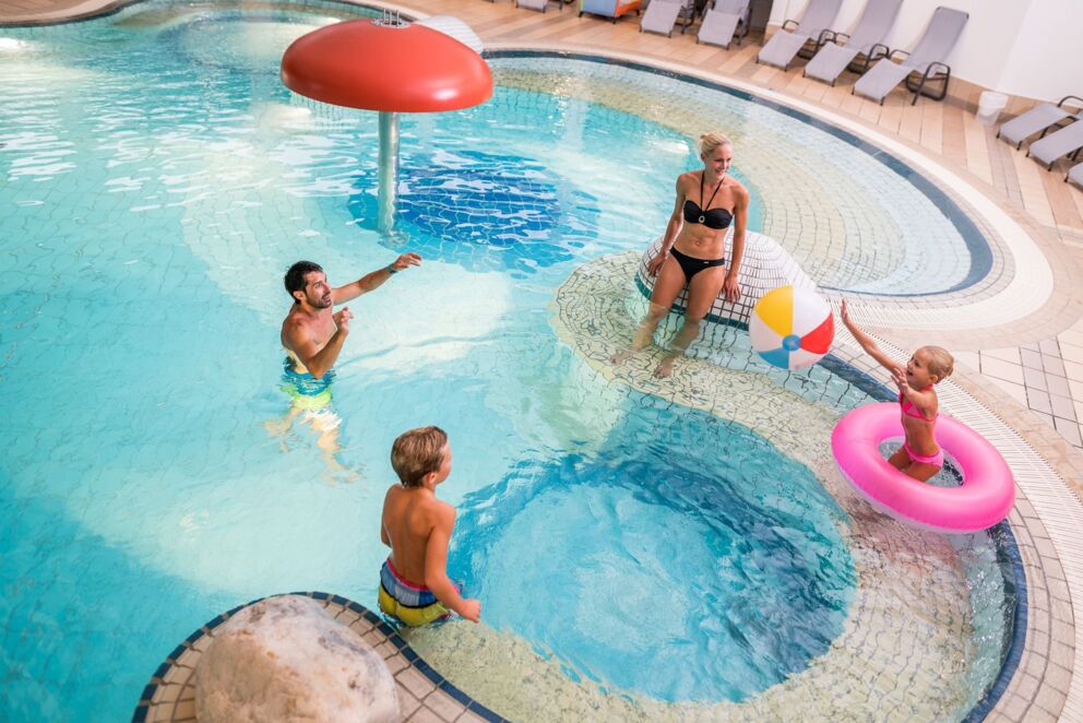 Eine Vierköpfige Familie die mit einen Wasserball in einen Becken in der Therme St Kathrein in Kärnten spielt.