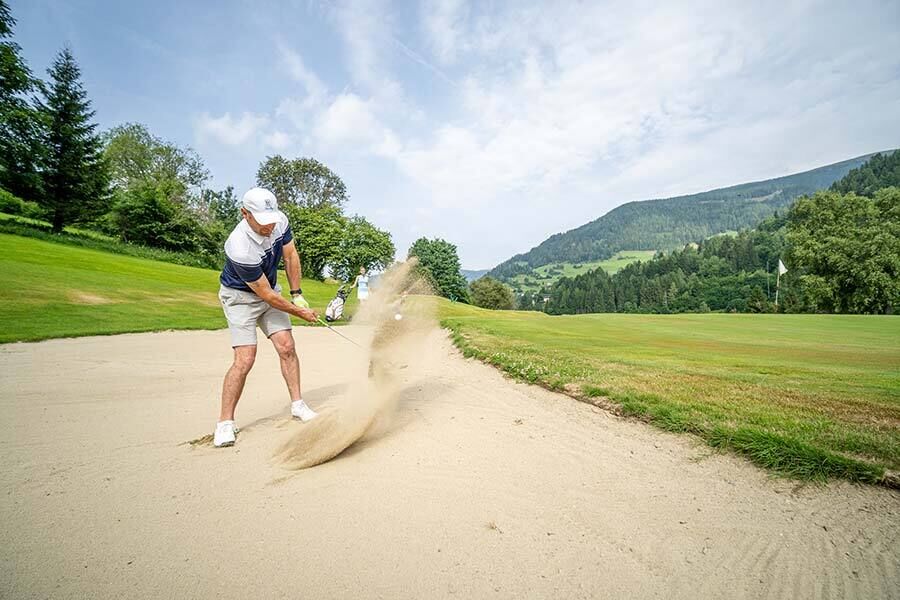 Un uomo effettua il suo tee shot sollevando sabbia