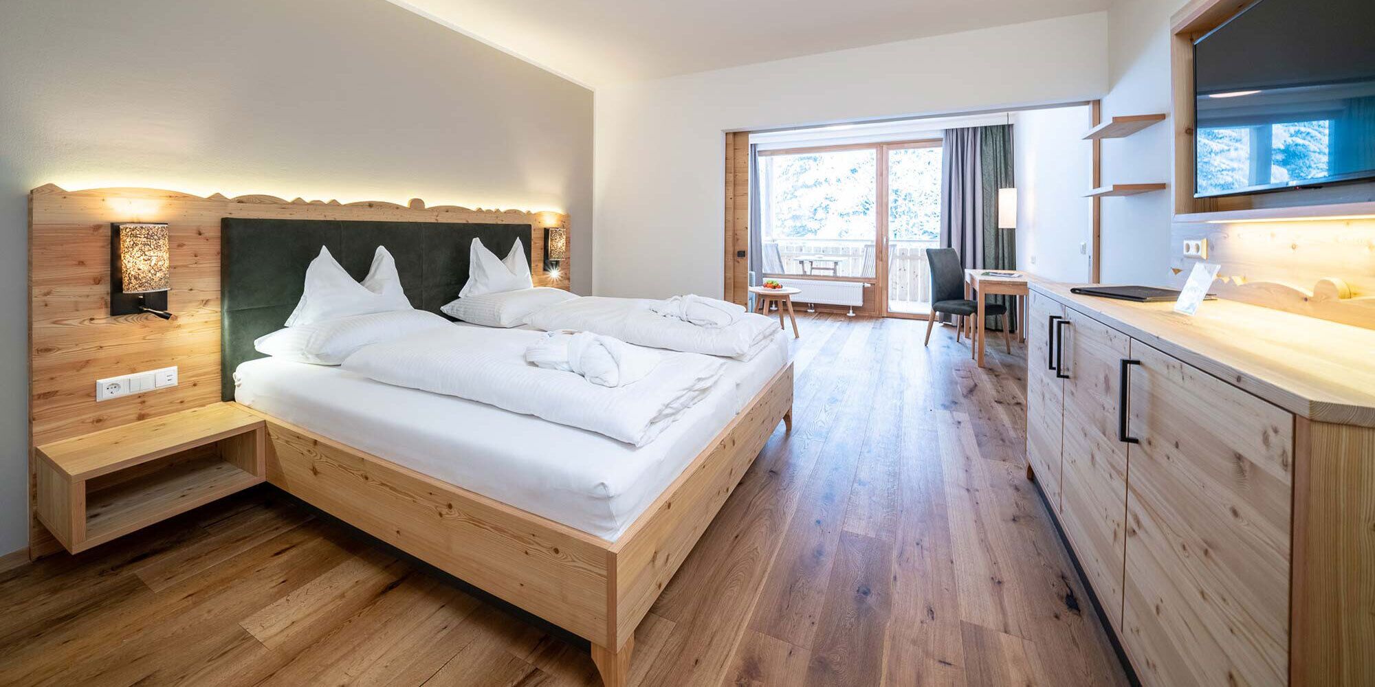 Ein großes und helles Hotelzimmer mit vielen Holzelementen und einem Balkon.