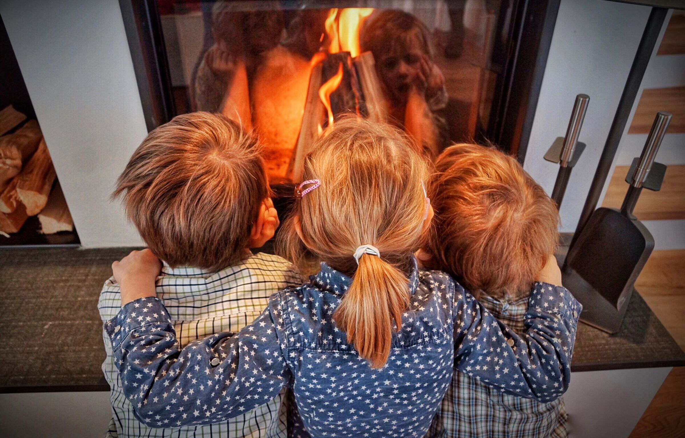 Drei Kinder schauen in den brennenden Ofen von den Chalets in Kärnten