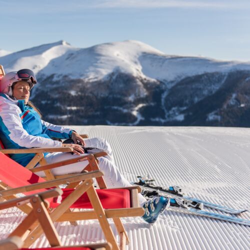 Eine Frau die eine Rast vom Skifahren macht und die Sonne im Liegestuhl genießt.