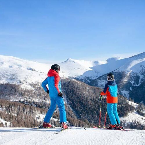 Father and son standing in ski equipment on a slope and marveling at nature in Carinthia