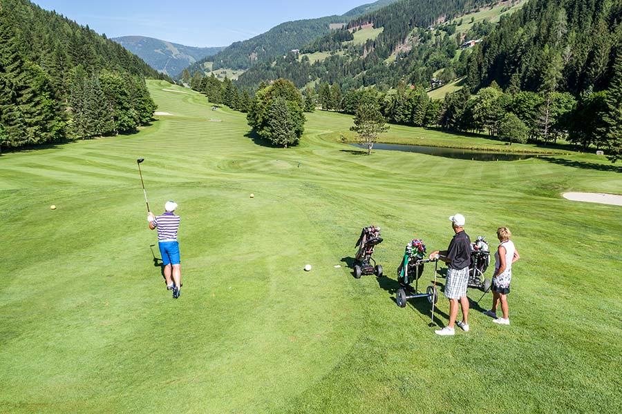 Un golfista che sta giocando sul campo verde di Bad Kleinkirchheim osserva altri due golfisti che stanno effettuando il tee di partenza.