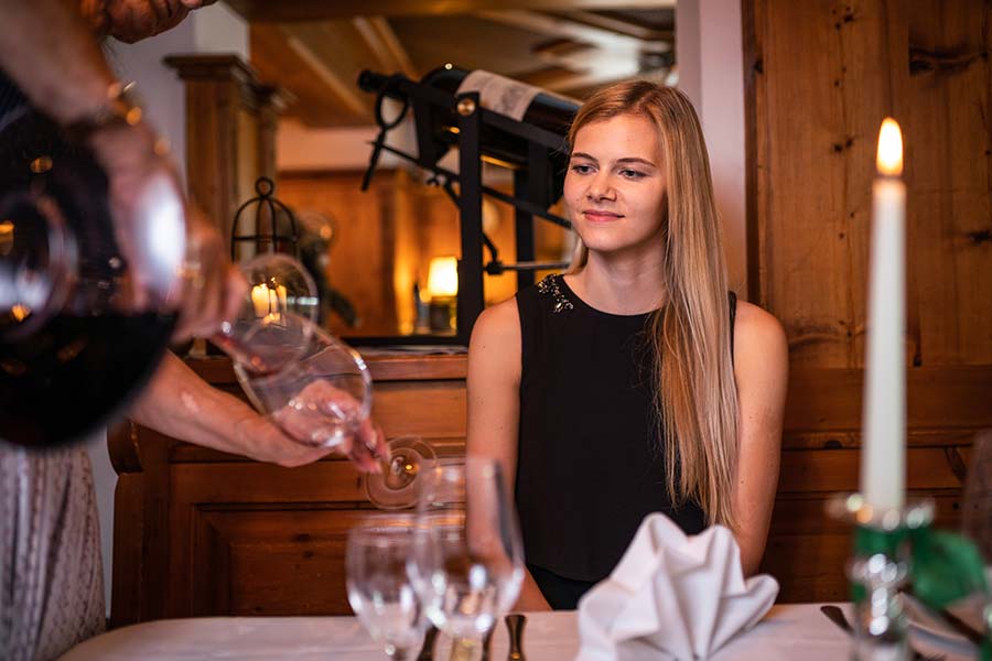 Eine Frau sitzt am Tisch und lässt sich im Hotel GUT Trattlerhof in Kärnten Wein einschenken