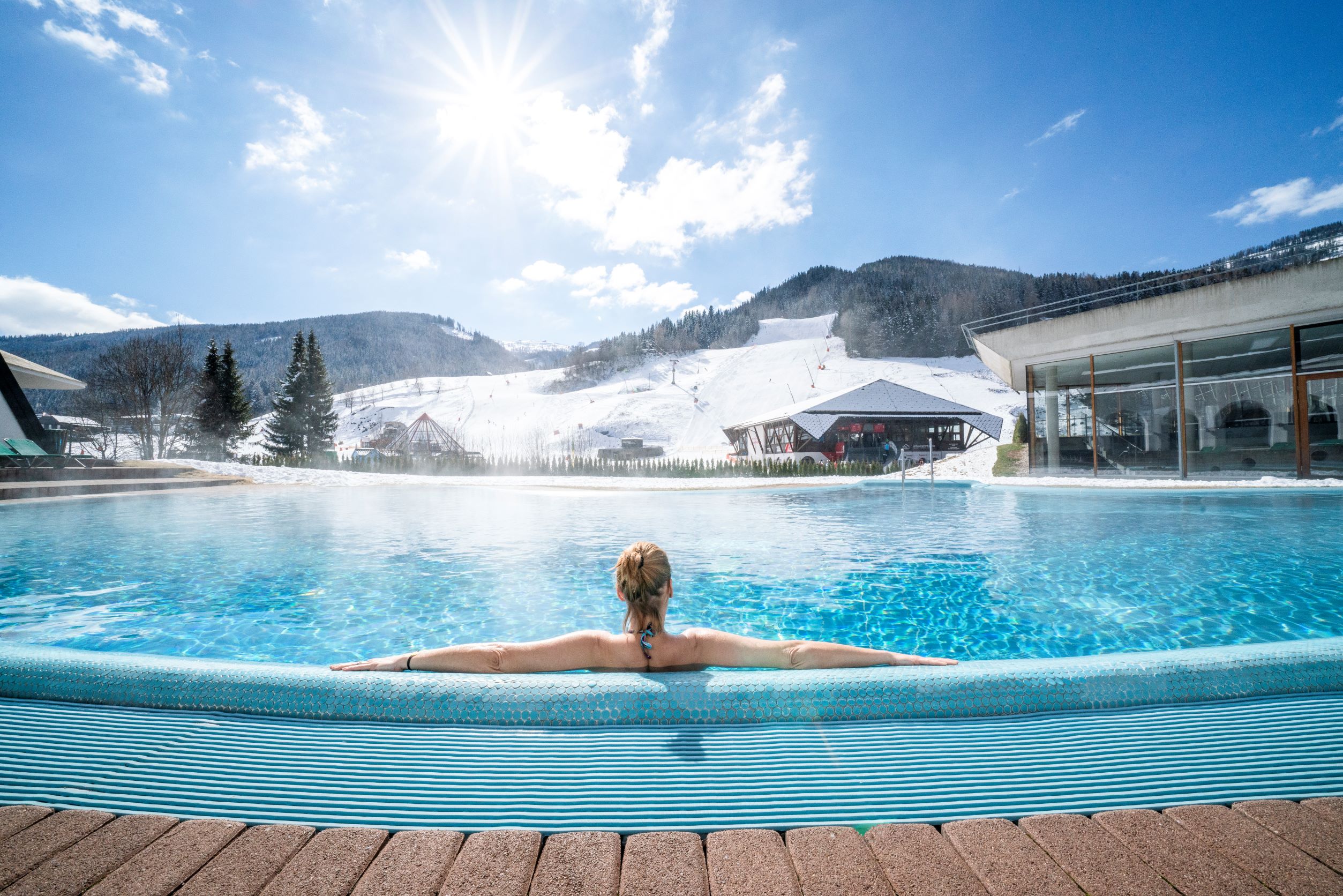 A woman sits in an outdoor pool and looks out over the slopes.